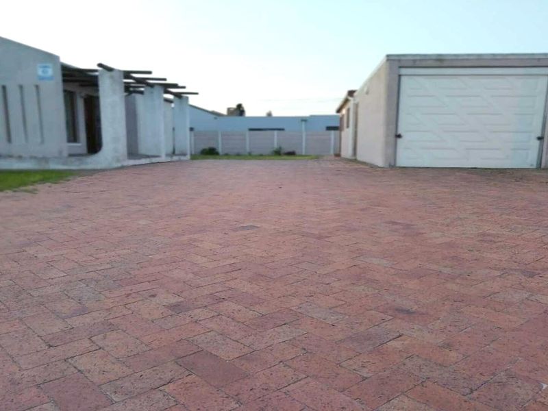 A paved driveway leading to a garage with an adjacent structure featuring a pergola and boundary wall.