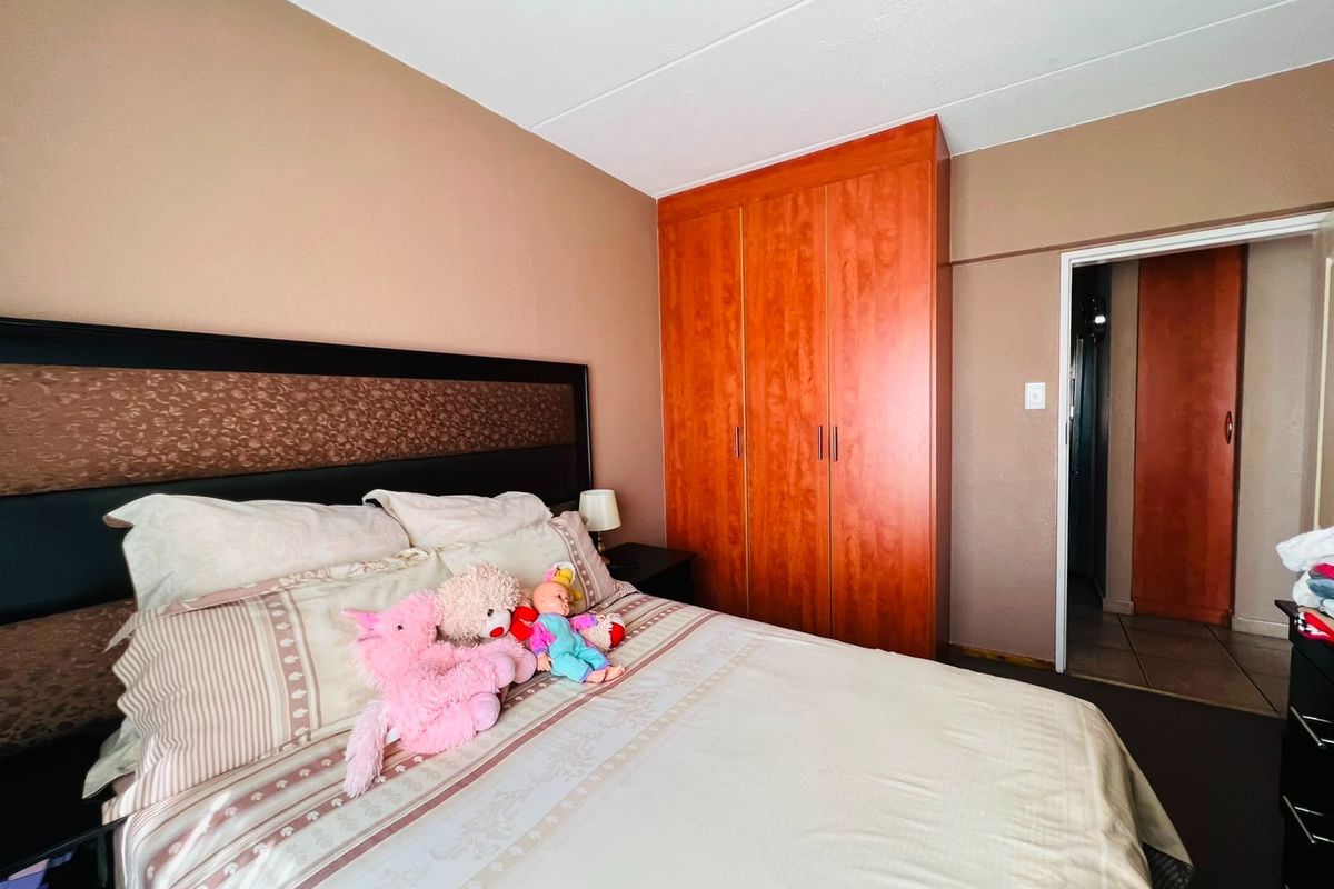 A bedroom featuring a built-in wooden wardrobe and neutral wall tones, providing a functional sleeping space with direct access to an adjoining room.