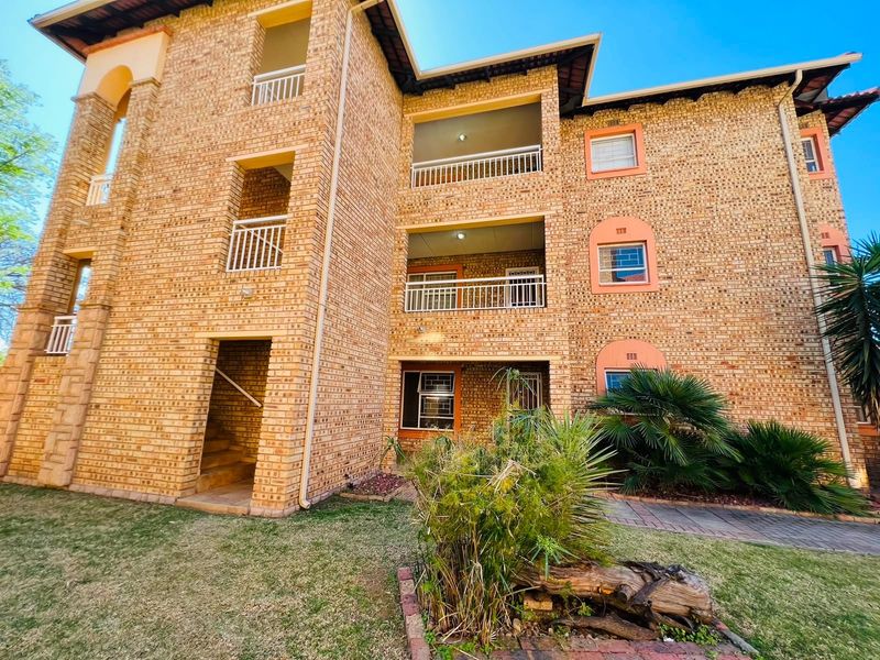 A multi-story apartment building exterior featuring face brick construction, private balconies, and a landscaped garden area with a paved walkway.
