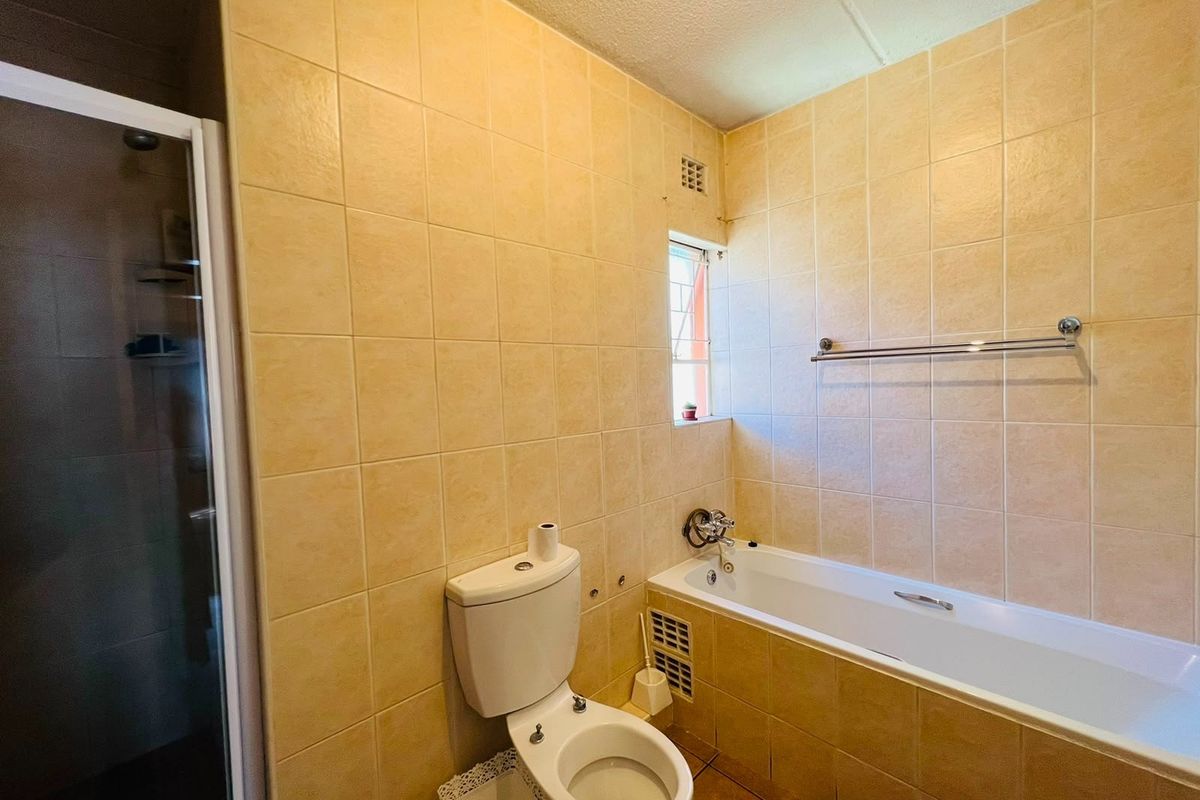 A functional bathroom featuring a bathtub, separate shower enclosure, and neutral wall tiling, offering a clean and practical layout.