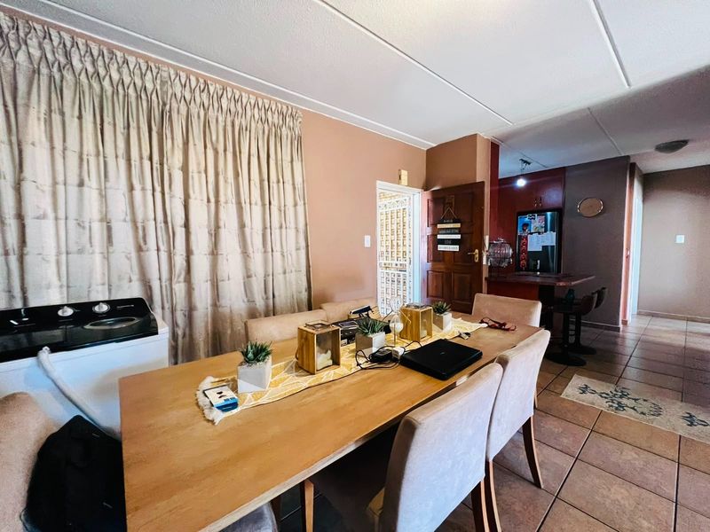 Open plan dining area featuring tiled flooring, flowing into a kitchen space with a breakfast bar and secure entrance door.