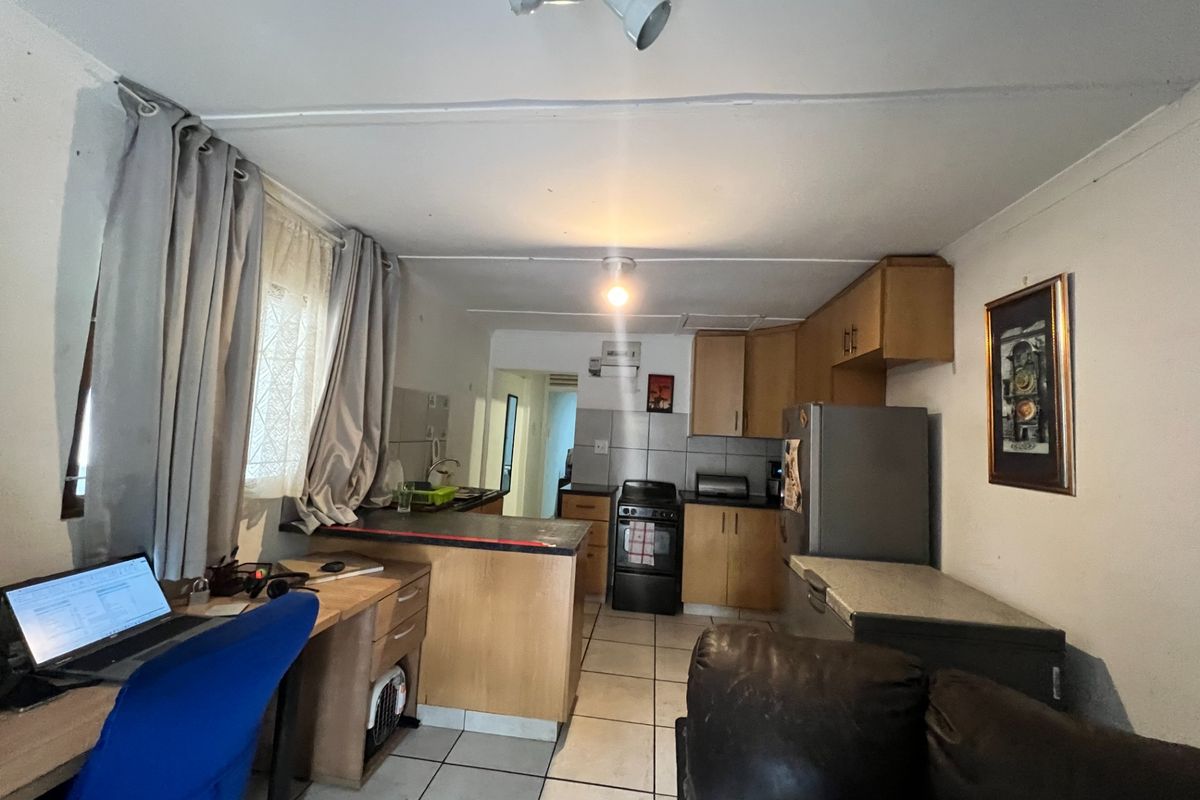 Open plan kitchen and living area featuring tiled flooring, wooden cabinetry, and a functional stove, offering a practical layout for daily living.