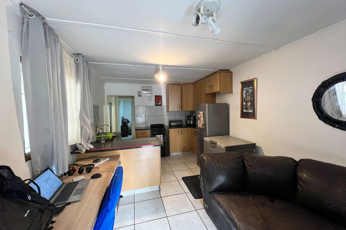 Open plan kitchen and living area featuring tiled flooring, wooden cabinetry, and a breakfast bar, offering a functional layout for daily living.