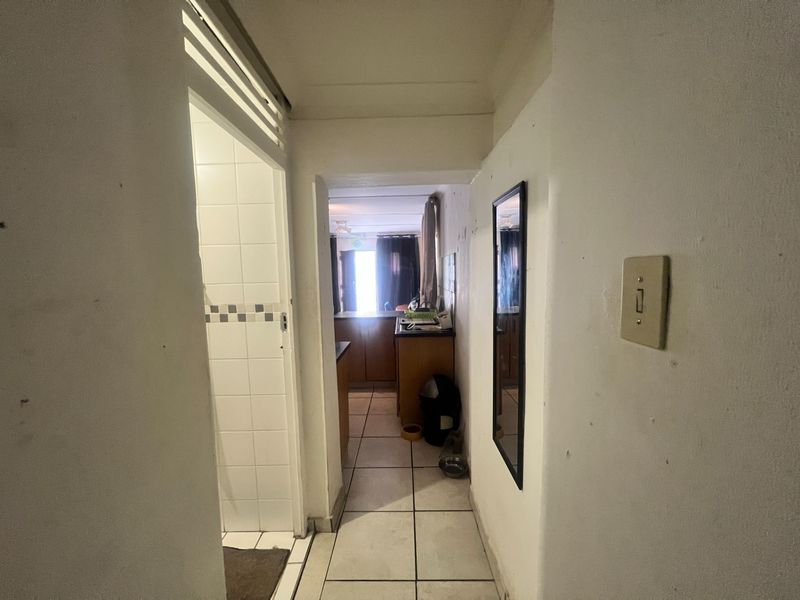 A narrow hallway with tiled flooring leading towards an open-plan living area, showing signs of wear on the walls and fixtures.