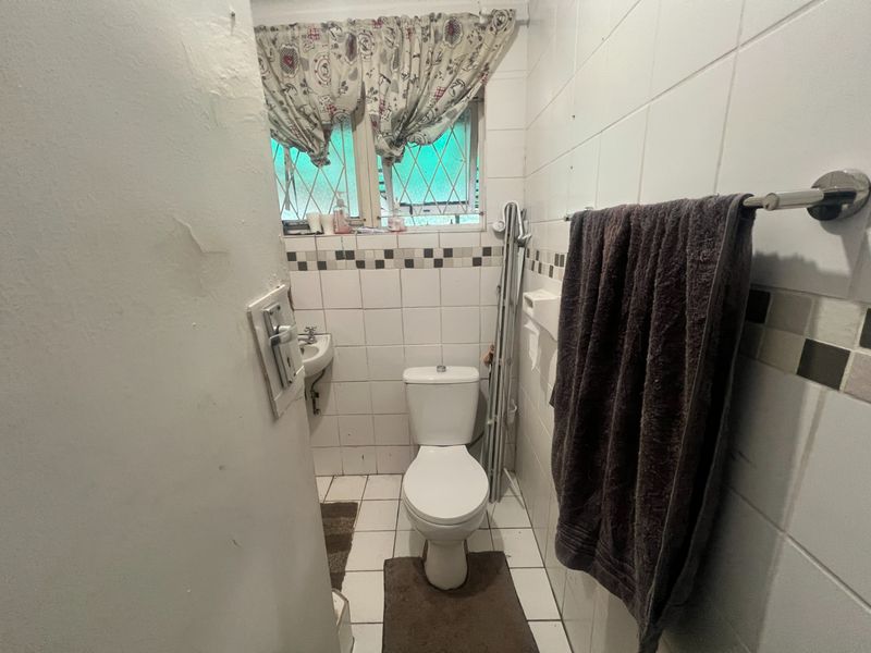 A compact bathroom featuring a standard toilet, wall-mounted basin, and tiled finishes, requiring some maintenance and cosmetic updates.