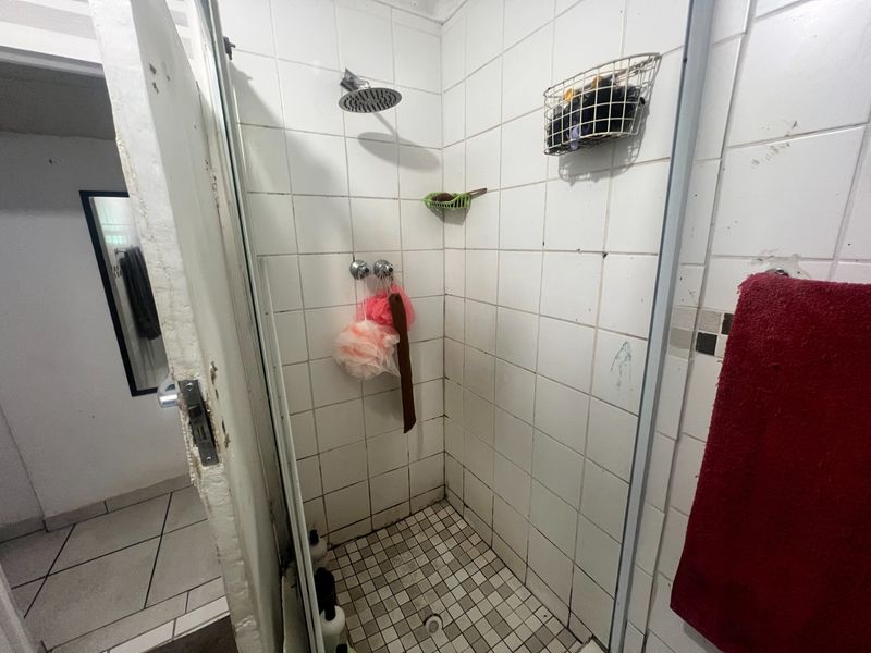 A compact shower stall featuring tiled walls and flooring, requiring maintenance to the door frame and grout.
