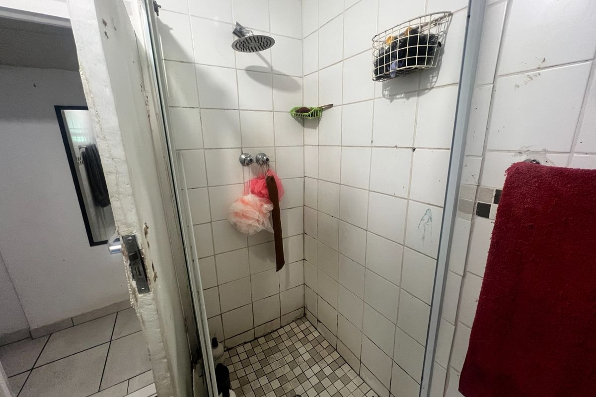 A compact shower stall featuring tiled walls and flooring, requiring maintenance to the door frame and grout.