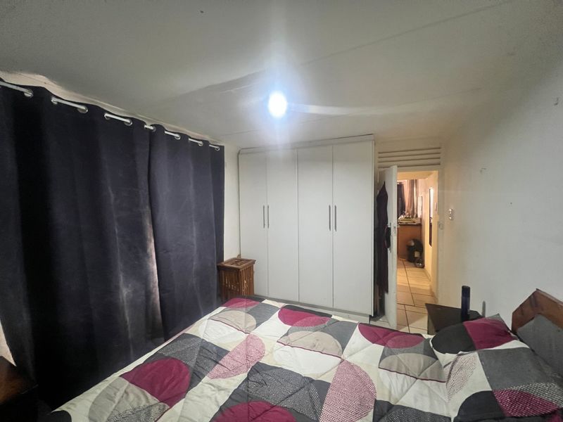 A bedroom featuring a built-in wardrobe and louvered door access to an adjacent room, showing signs of wear on the walls and ceiling.