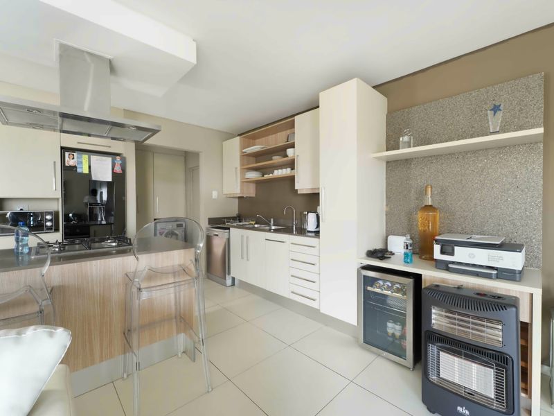 Modern kitchen featuring sleek cabinetry, stone countertops, integrated gas hob, extractor fan, and tiled flooring in an open-plan layout.