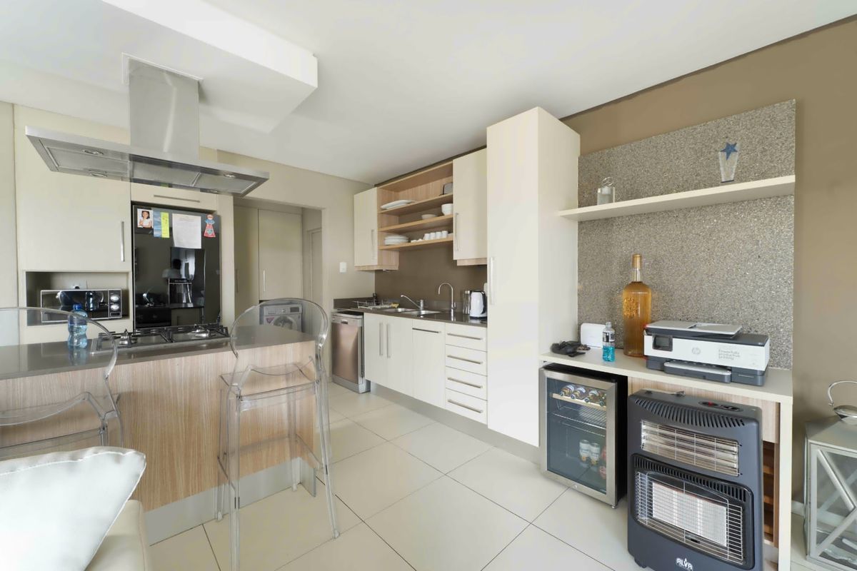 Modern kitchen featuring sleek cabinetry, stone countertops, integrated gas hob, extractor fan, and tiled flooring in an open-plan layout.