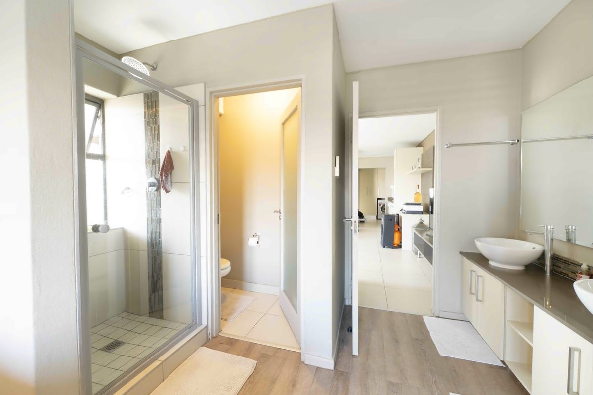 Modern bathroom featuring a glass-enclosed shower, dual vessel sinks on a vanity cabinet, and a separate toilet area with neutral finishes.