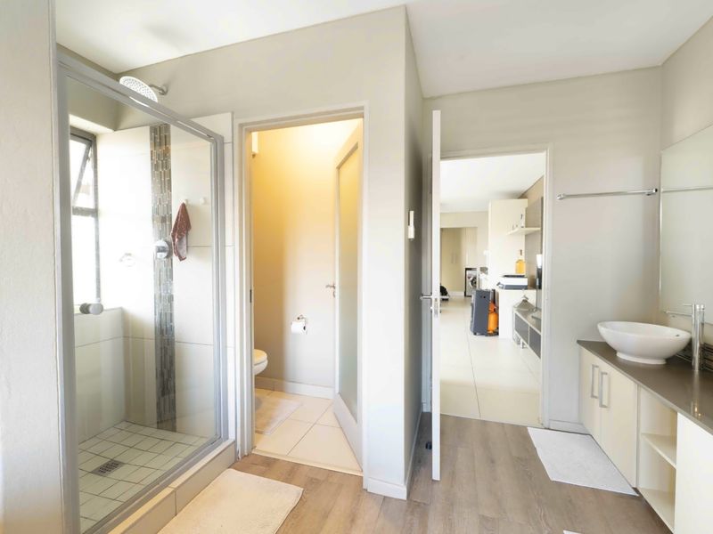 Modern bathroom featuring a glass-enclosed shower, dual vessel sinks on a vanity cabinet, and a separate toilet area with neutral finishes.