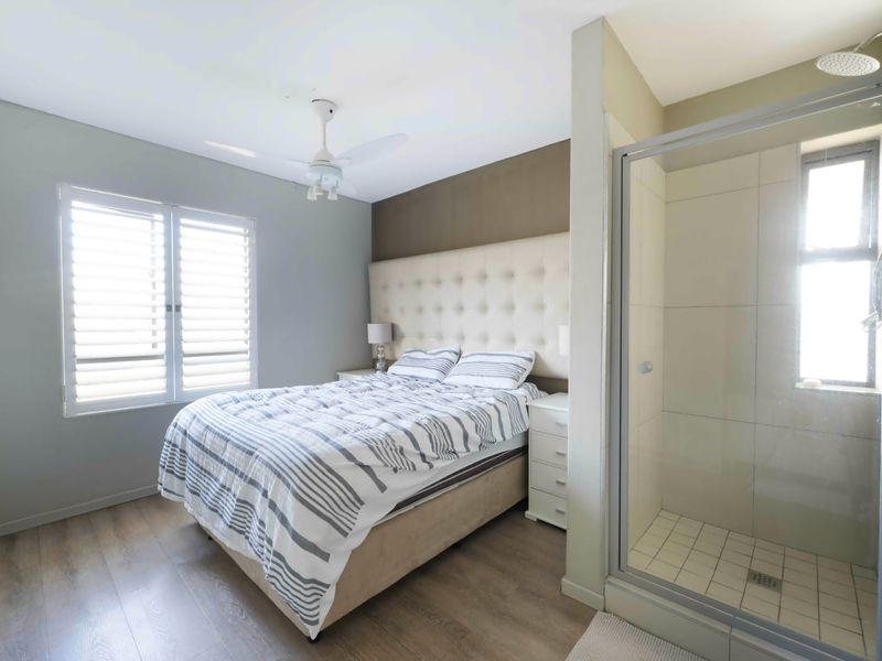 A well-maintained bedroom featuring laminate flooring, plantation shutters, a ceiling fan, and an integrated en-suite shower with tiled finishes.