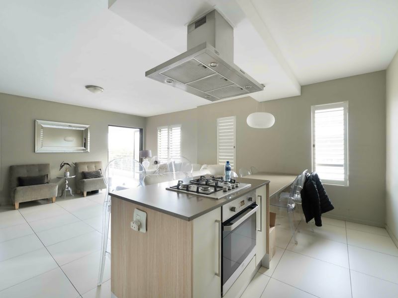 Open-plan living area featuring a modern kitchen island with gas hob, built-in oven, extractor fan, and neutral tiled flooring throughout.