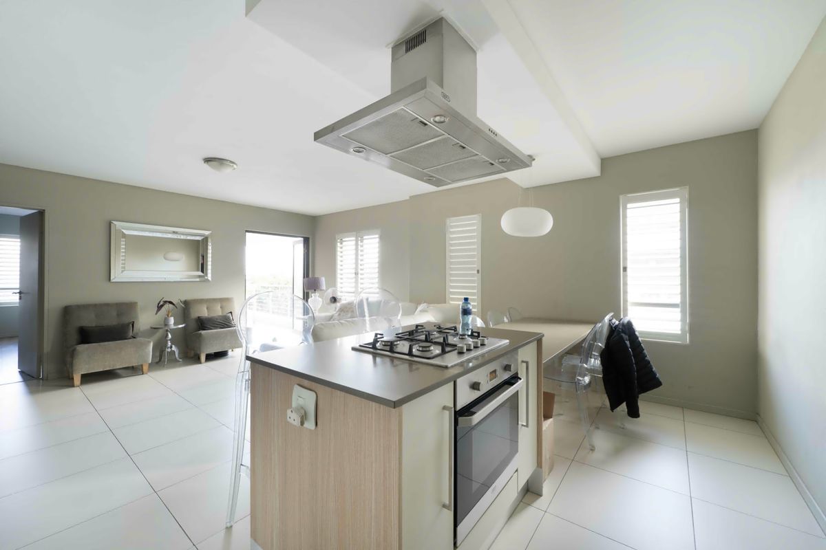 Open-plan living area featuring a modern kitchen island with gas hob, built-in oven, extractor fan, and neutral tiled flooring throughout.