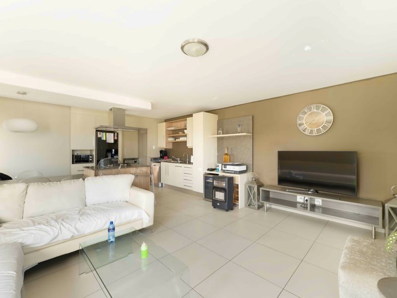 An open-plan living and kitchen area featuring tiled flooring, modern cabinetry, and a functional kitchen layout with integrated appliances.