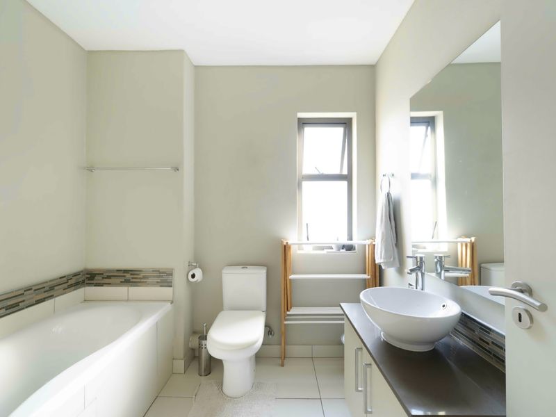 A clean, modern bathroom featuring a built-in bathtub, a vessel sink on a vanity cabinet, and a large wall-mounted mirror.