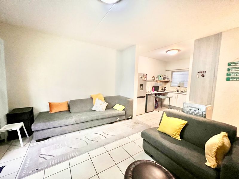 An open-plan living area featuring tiled flooring and a compact kitchen with built-in cabinetry and sink.