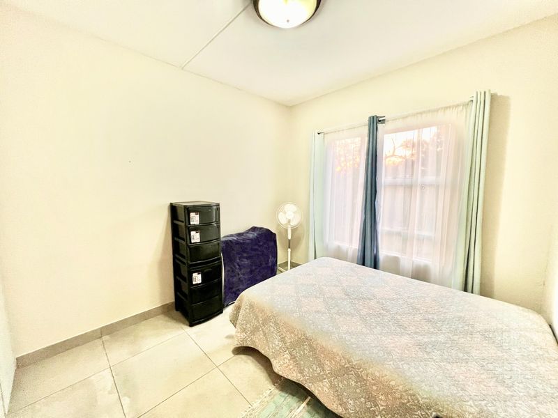 A simple bedroom featuring neutral tiled flooring and a central ceiling light fixture, providing a functional space with natural light from the window.