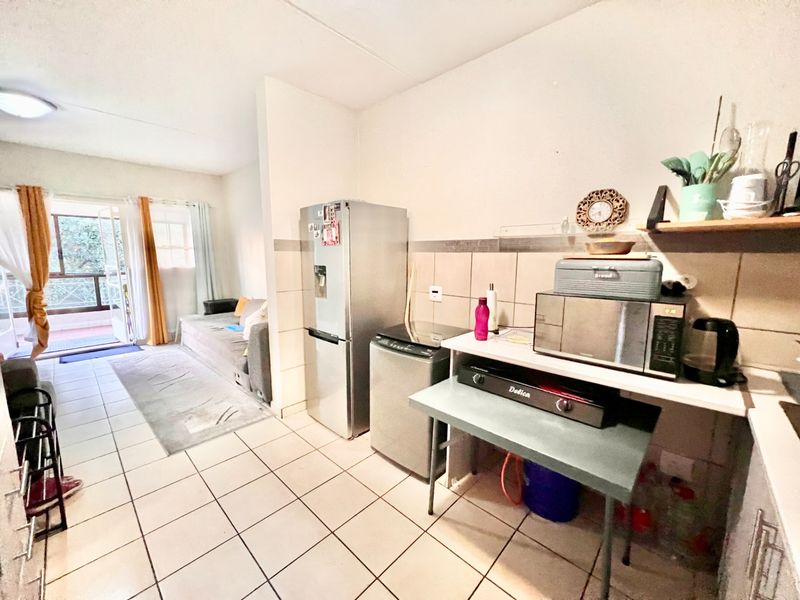 Open-plan living area featuring tiled flooring and a kitchen nook with tiled splashback, leading directly to a balcony through a sliding door.