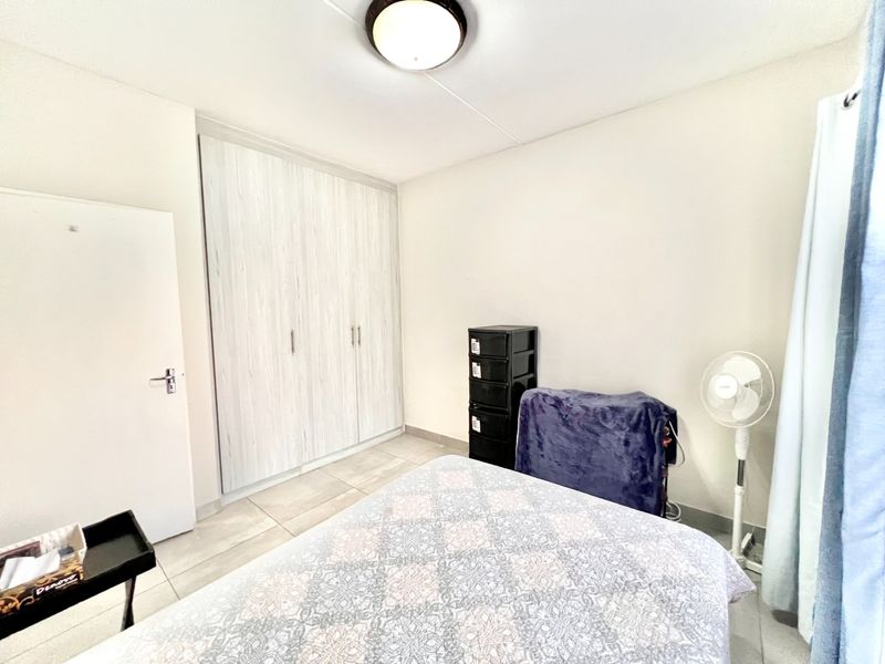 A functional bedroom featuring built-in cupboards, tiled flooring, and a neutral color palette, offering a clean and practical living space.