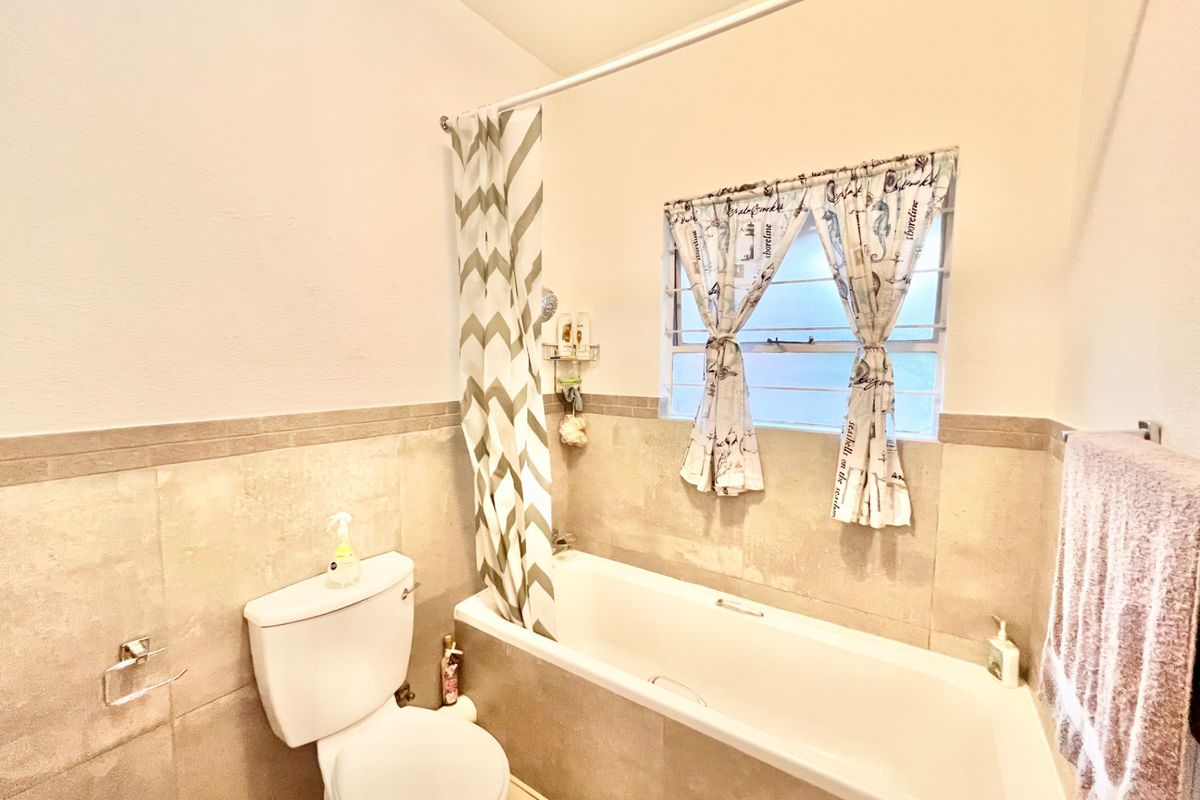 A functional bathroom featuring neutral wall and floor tiling, a standard bathtub with shower curtain, and a louvered window for ventilation.