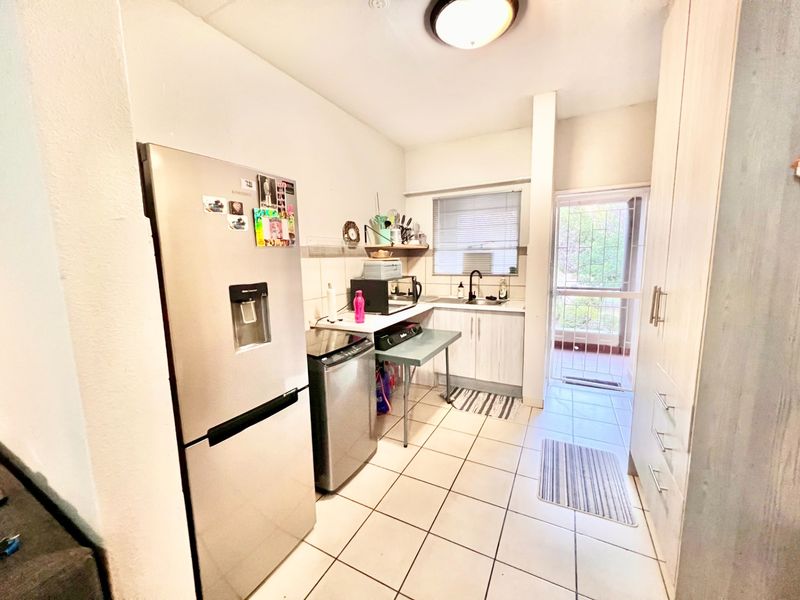 A functional kitchen featuring tiled flooring, built-in cabinetry, and direct access to an outdoor area through a security gate.