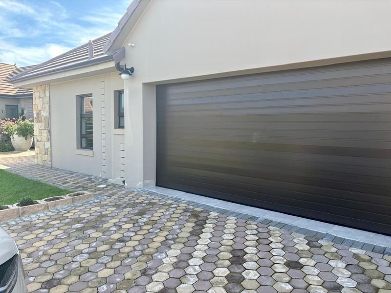 Front exterior view of the property featuring a modern sectional garage door, stone cladding accents, and a paved driveway.