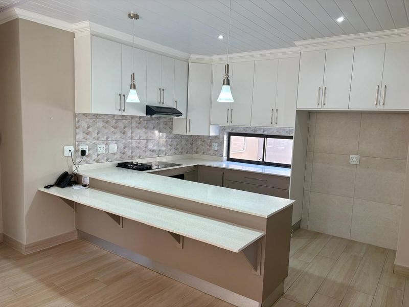 Modern kitchen featuring white cabinetry, stone countertops, a breakfast bar, gas hob, and stylish tiled backsplash with integrated lighting.