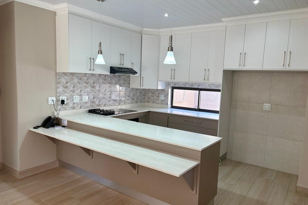 Modern kitchen featuring white cabinetry, stone countertops, a breakfast bar, gas hob, and stylish tiled backsplash with integrated lighting.
