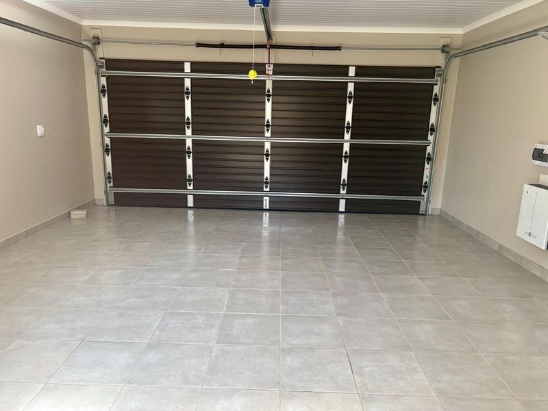 A clean, well-maintained double garage featuring tiled flooring, a sectional garage door, and an integrated electrical distribution board.