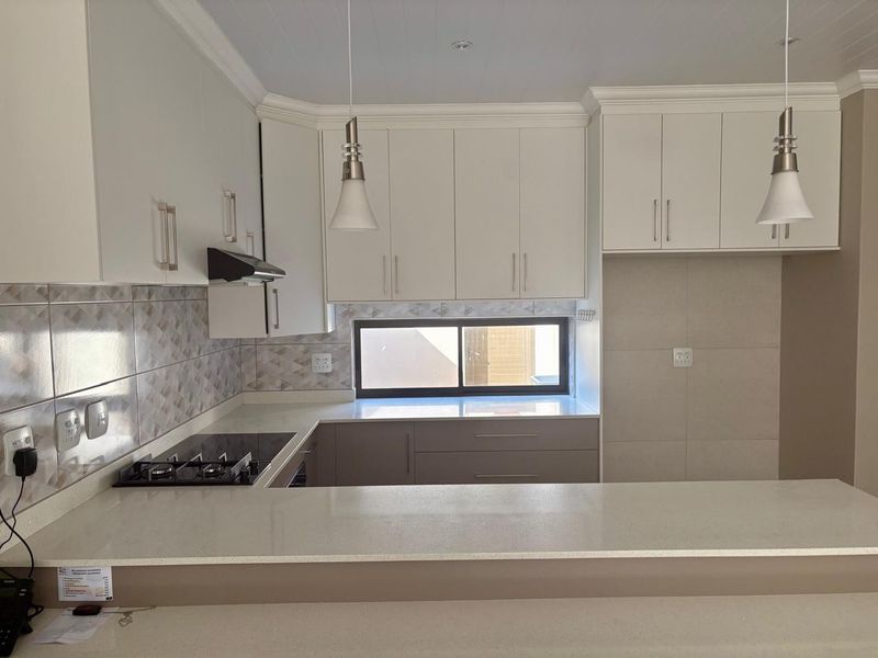 Modern kitchen featuring white cabinetry, stone countertops, a gas hob with extractor fan, and a breakfast bar, presented in excellent condition.