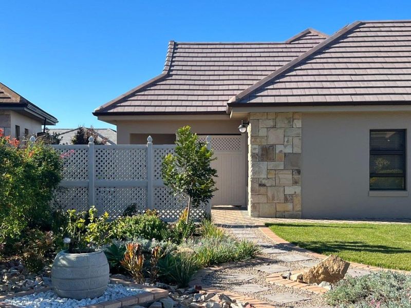 A well-maintained front exterior featuring stone cladding, a tiled roof, and a neatly landscaped garden with a paved walkway leading to the entrance.
