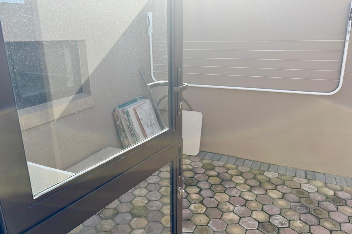 A small paved rear courtyard area featuring a wall-mounted clothesline and access via an aluminium door.