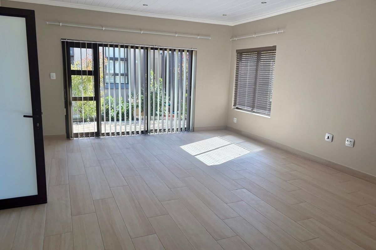 A bright, empty living room featuring modern wood-look tile flooring, a tongue and groove ceiling with recessed lighting, and access to an outdoor area.