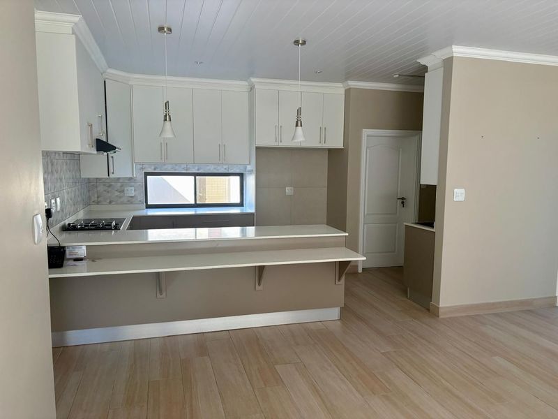 Modern kitchen featuring white cabinetry, stone countertops, a breakfast bar, gas hob, and tiled flooring in an open-plan layout.