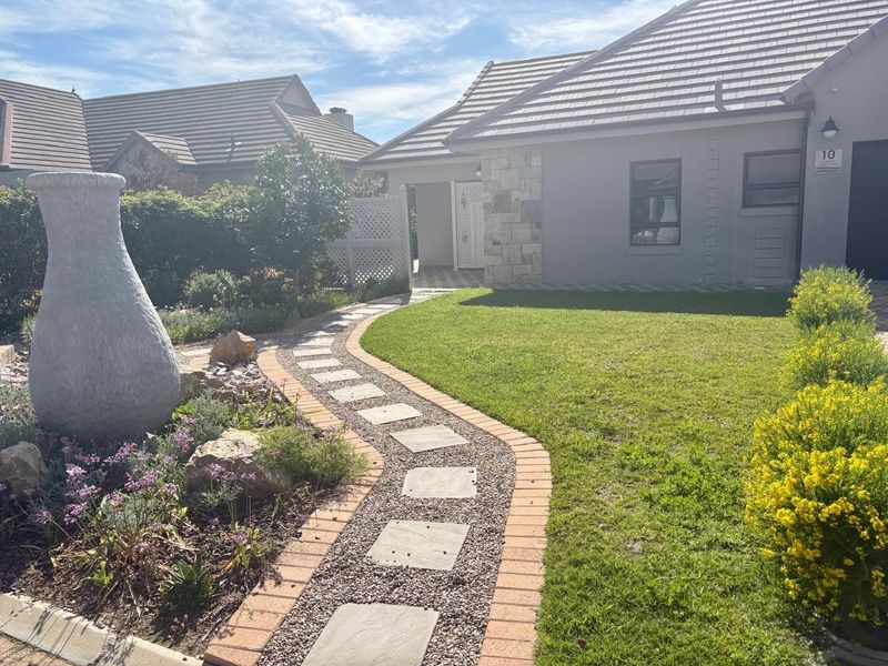 A well-maintained front garden featuring a stone-paved walkway, manicured lawn, and decorative stone water feature leading to the home entrance.