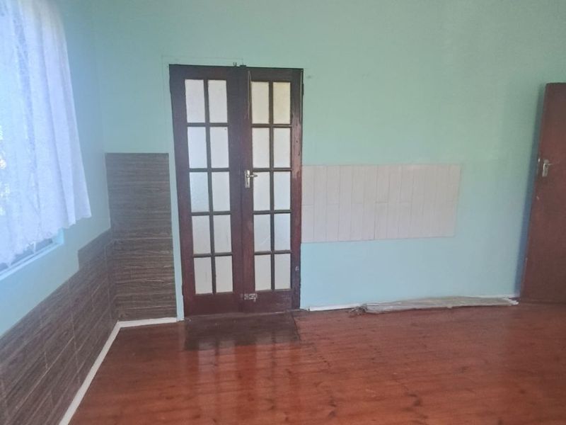An empty living room featuring timber flooring, french doors, and partial wall tiling, offering a blank canvas for renovation and interior design.