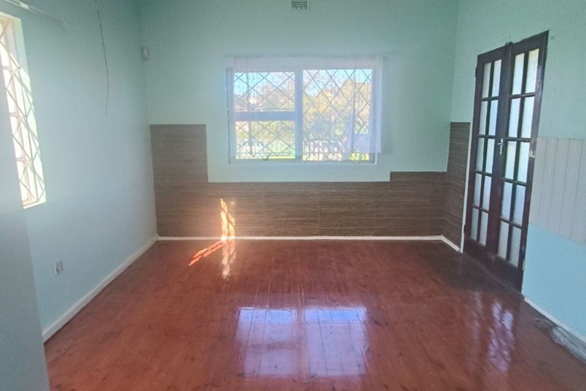 An empty living room featuring polished timber flooring, security bars on windows, and classic french doors, offering a blank canvas for renovation.