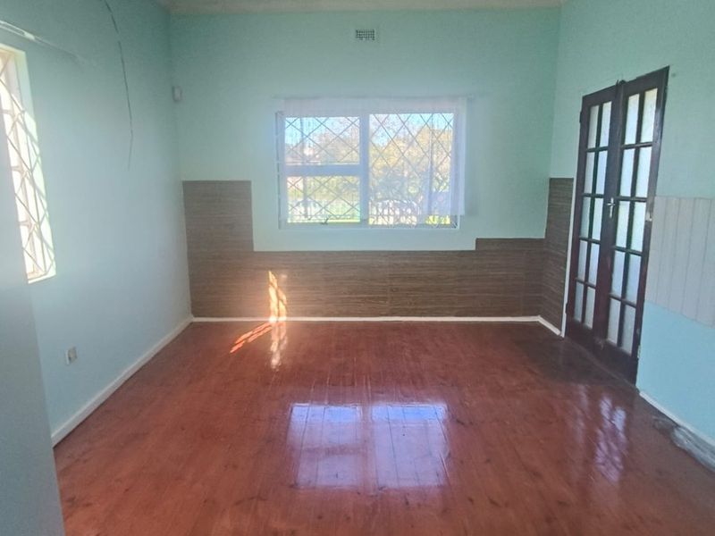 An empty living room featuring polished timber flooring, security bars on windows, and classic french doors, offering a blank canvas for renovation.