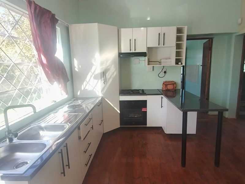 A functional kitchen featuring white cabinetry, a built-in oven with hob, double sink, and a breakfast bar, set against wooden flooring.