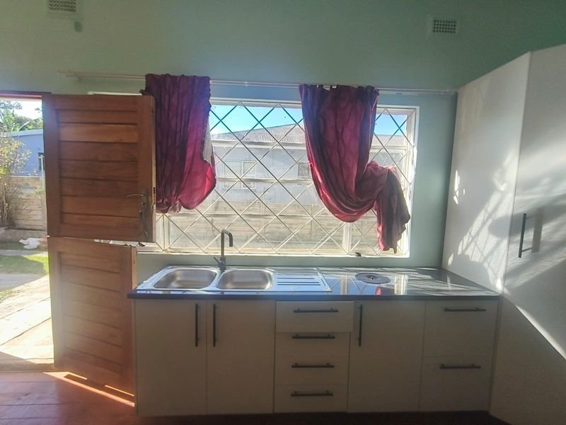 A functional kitchen area featuring modern white cabinetry, a double sink with a mixer tap, and a large window with security bars.