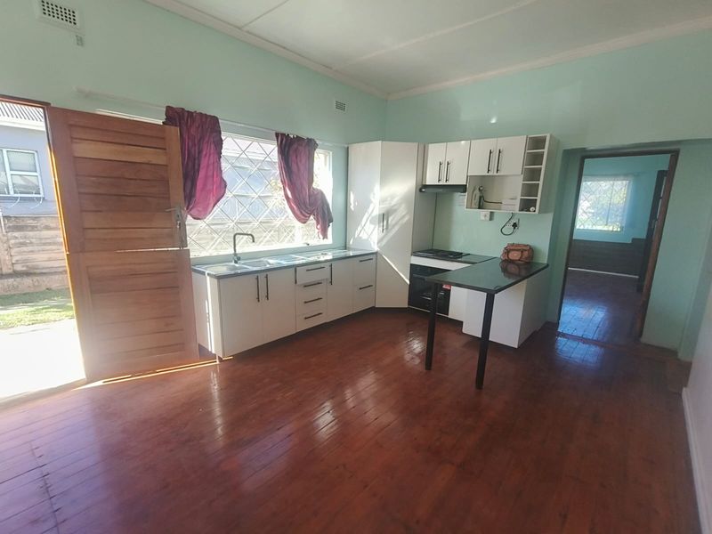 A functional kitchen featuring white cabinetry, integrated appliances, and timber flooring, with direct access to the exterior through a security door.