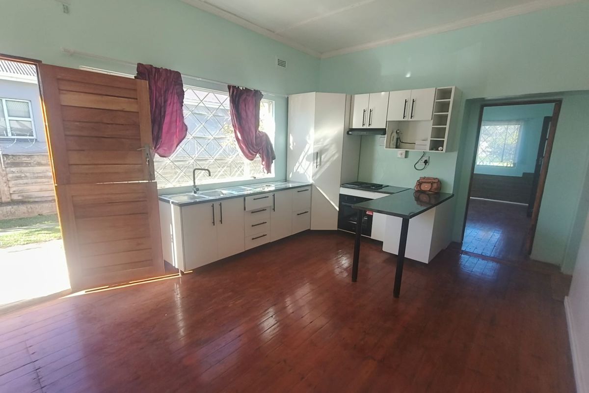 A functional kitchen featuring white cabinetry, integrated appliances, and timber flooring, with direct access to the exterior through a security door.