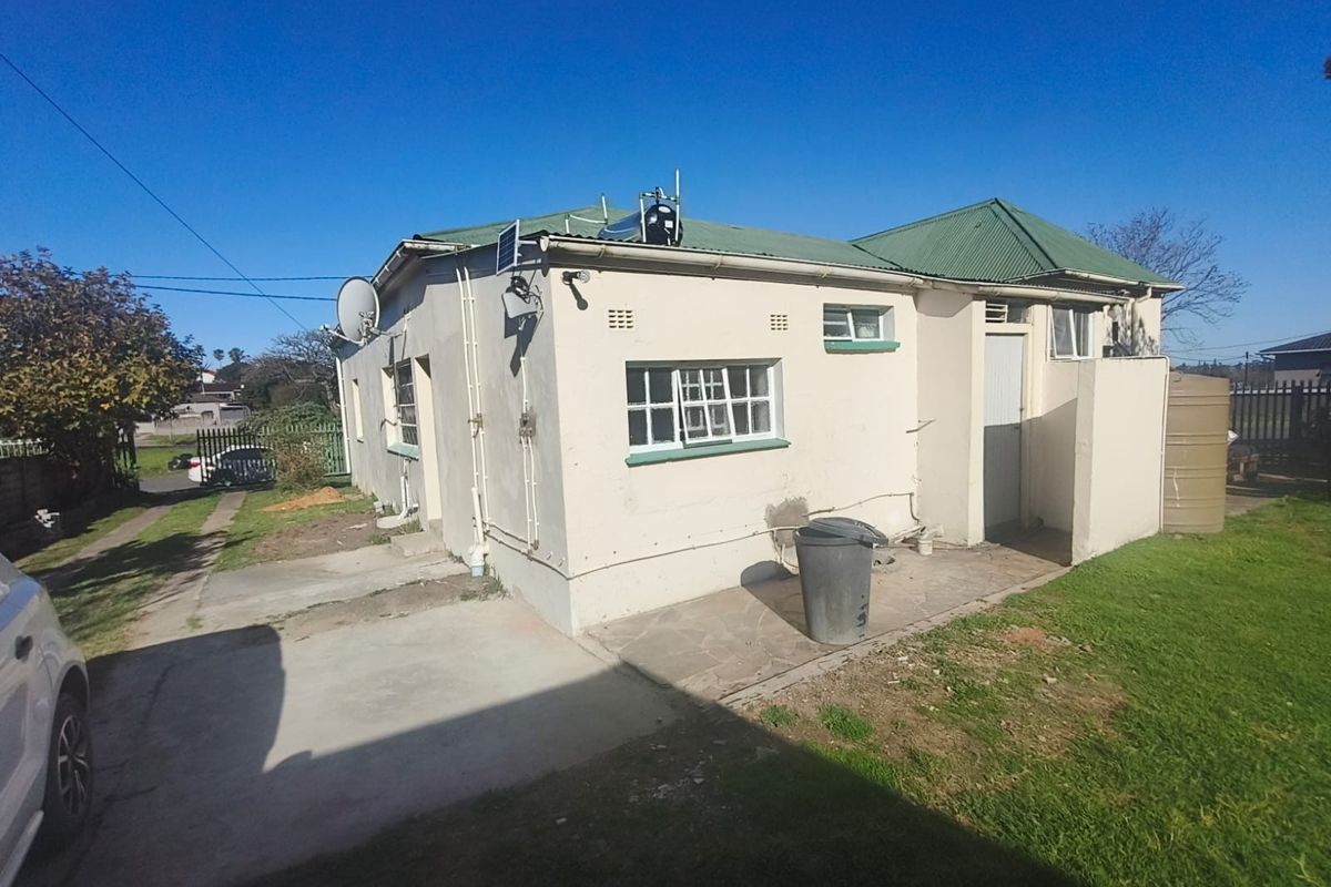 Rear view of the property showing the exterior facade, corrugated metal roof, solar water heating system, and paved patio area.
