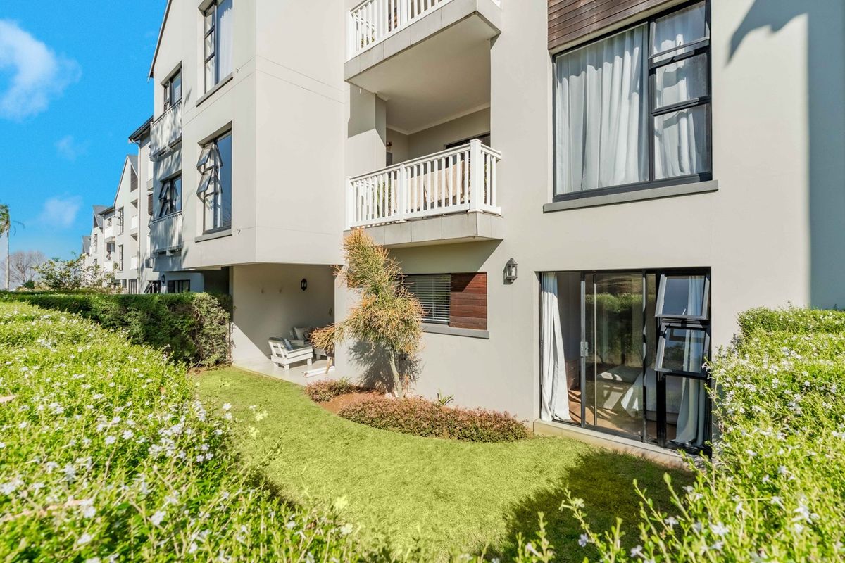 Rear view of a modern apartment building featuring private balconies, sliding glass doors, and a well-maintained ground-floor garden area.