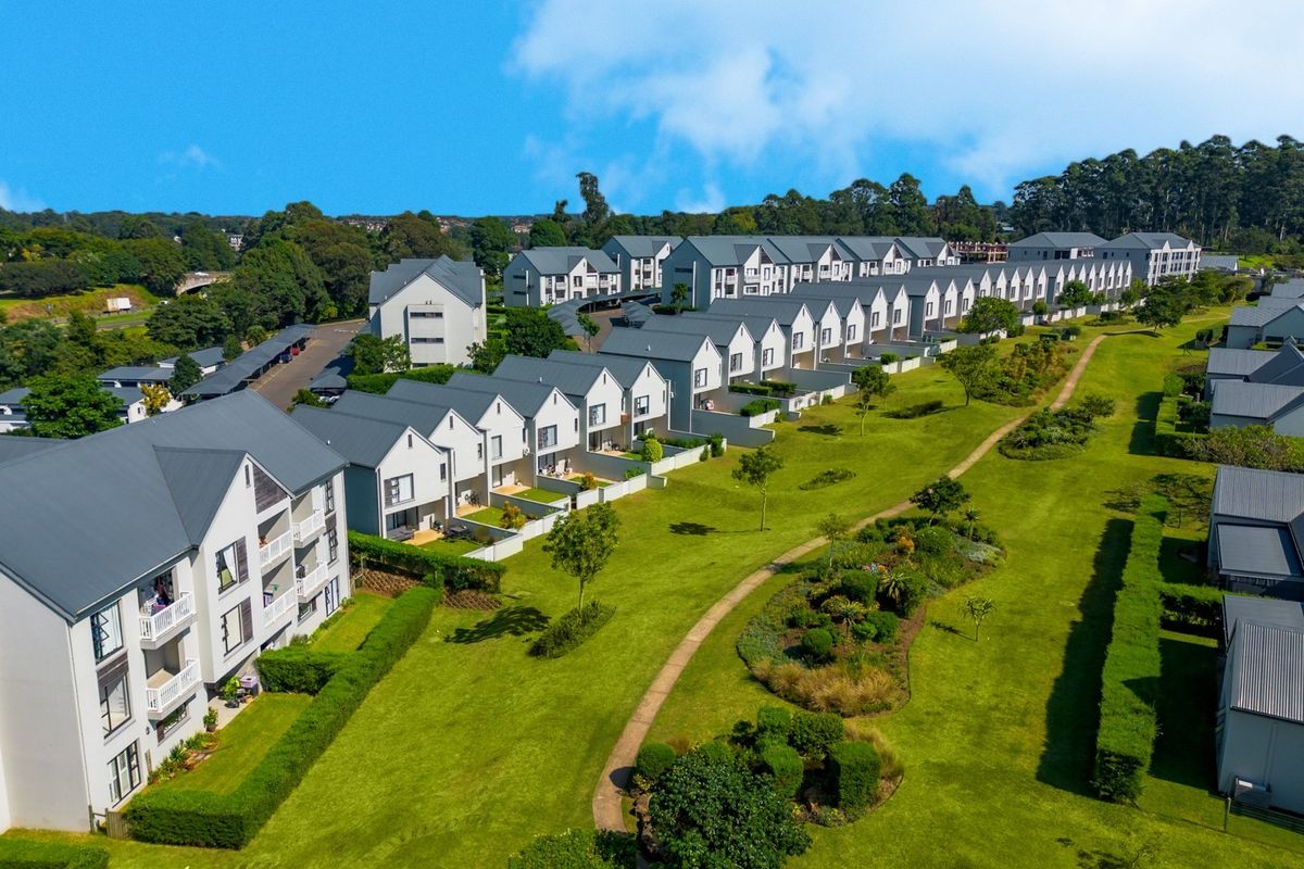 Aerial view of a modern residential apartment complex featuring uniform pitched-roof buildings, extensive landscaped communal gardens, and paved walkways.