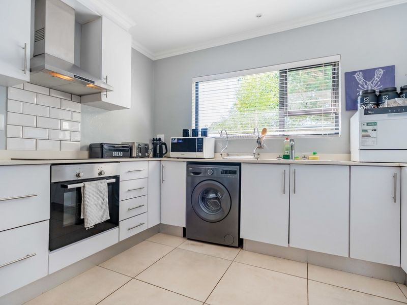 A well-maintained kitchen featuring white cabinetry, a subway tile backsplash, built-in oven, extractor fan, and integrated laundry appliance space.