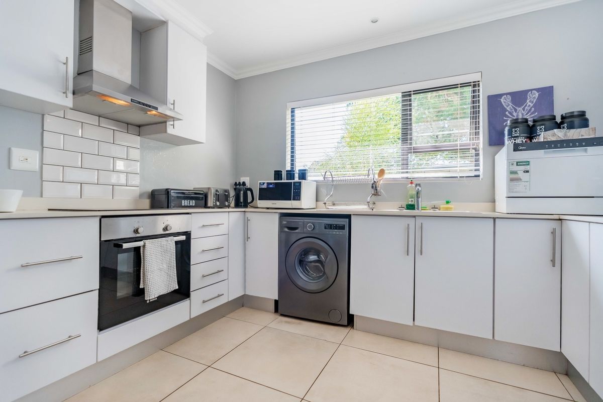 A well-maintained kitchen featuring white cabinetry, a subway tile backsplash, built-in oven, extractor fan, and integrated laundry appliance space.