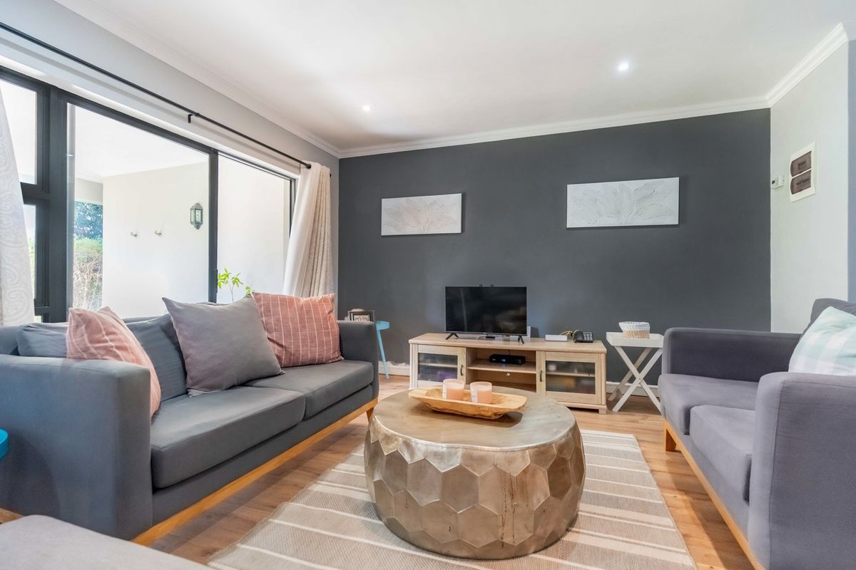 A well-maintained living room featuring laminate flooring, recessed downlights, and a large sliding glass door providing access to the outdoor area.